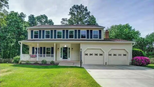 Une maison à deux étages avec un porche à l’avant, un garage à deux portes et une pelouse bien entretenue.