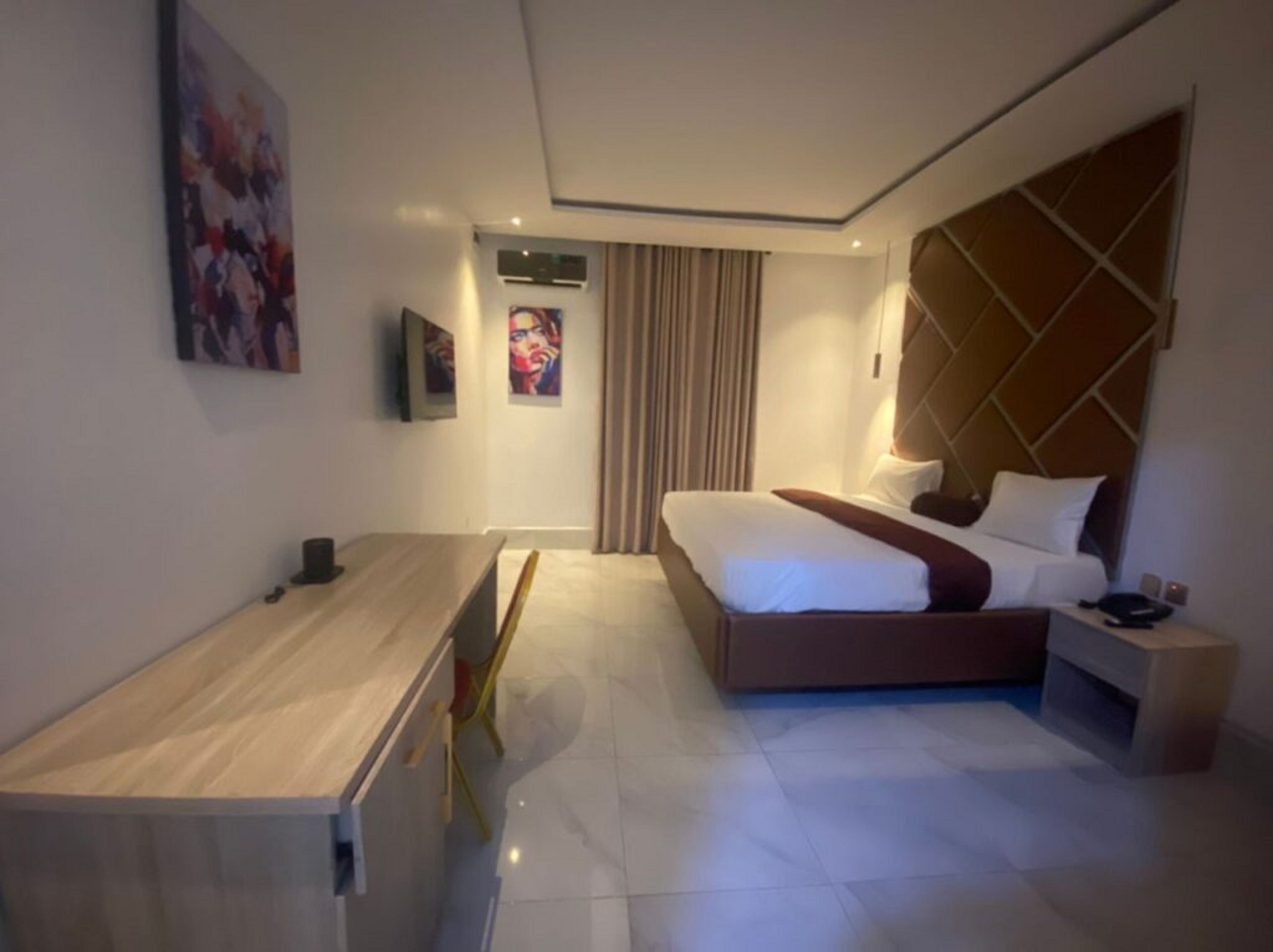 A modern hotel room with a bed, bedside table, and a desk with a chair.
