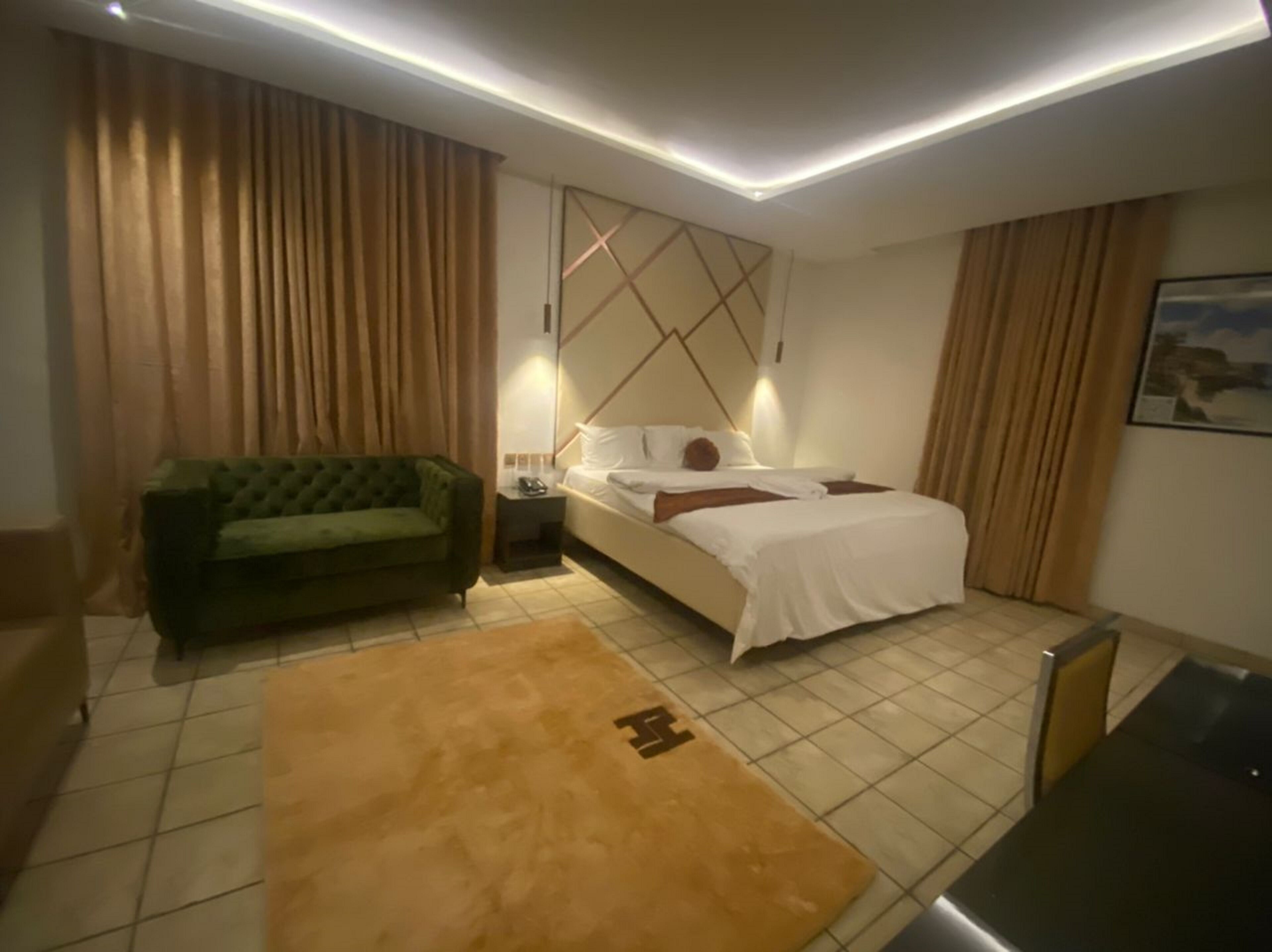 A hotel room with a bed, a green sofa, a small table, and a TV.