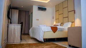 A modern hotel room with a bed, a desk, a television, and an air conditioning unit. - Hopeland Hotels (Port Harcourt)