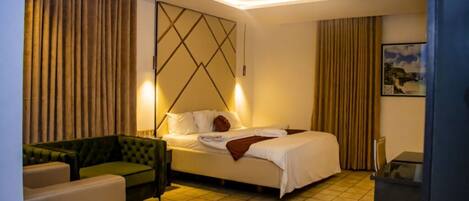 Una habitación de hotel con una cama, un sillón verde, una mesita y un cuadro en la pared.