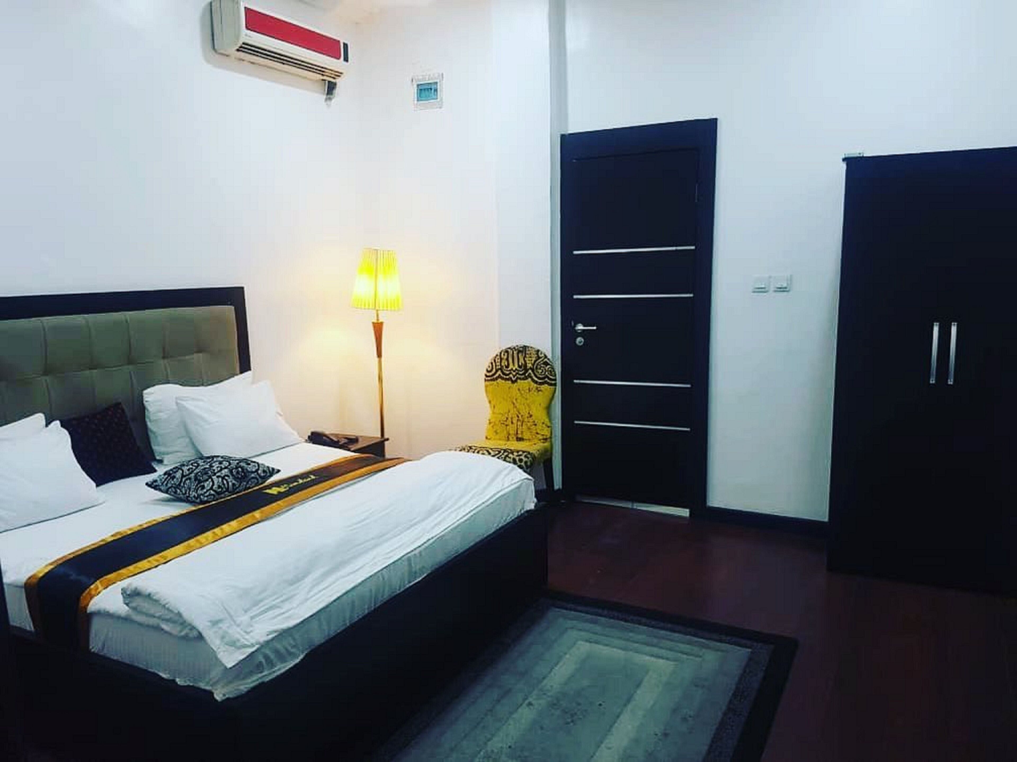 A hotel room with a bed, a bedside lamp, a wardrobe, and a door.