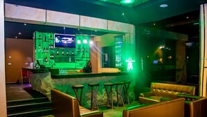 A bar area with a green-lit bar counter, multiple stools, and leather seating. - Hopeland Hotels (Port Harcourt)