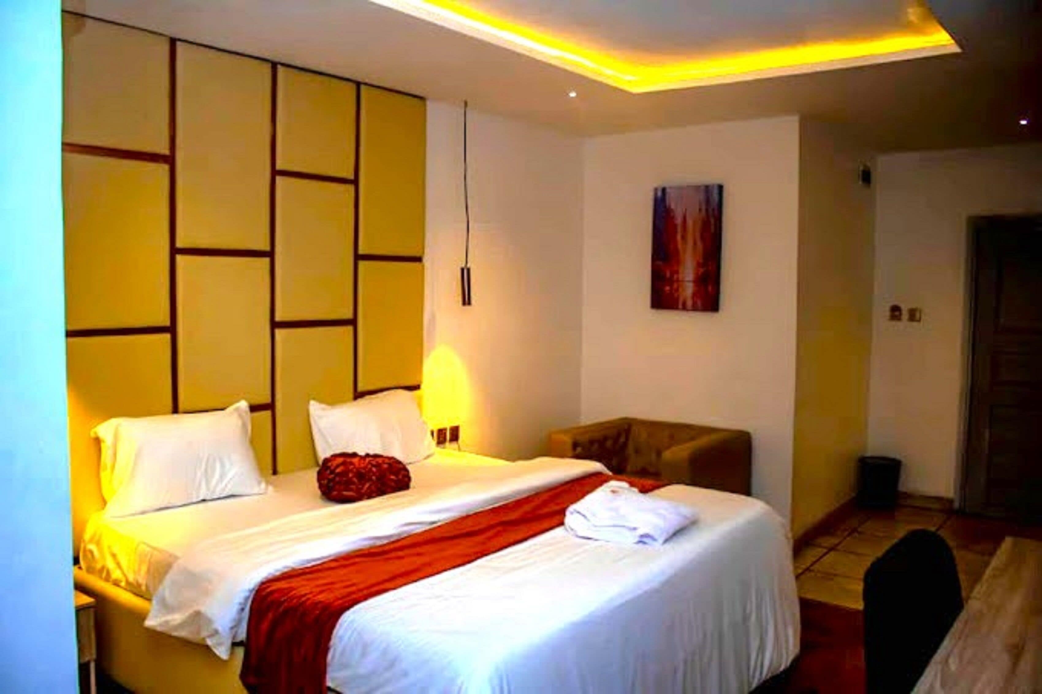 A hotel room with a bed, a chair, a painting on the wall, and a door.