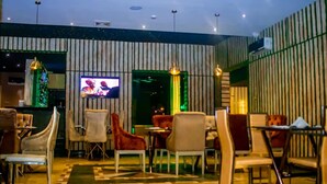 A restaurant with a modern interior, featuring striped walls, multiple seating areas, and a television screen. - Hopeland Hotels (Port Harcourt)
