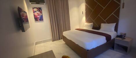 A hotel room with a bed, bedside table, chair, and a painting on the wall.