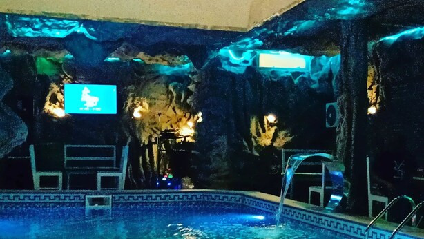 An indoor swimming pool with clear water, a tiled floor, and a rock-like wall in the background. - Hopeland Hotels (Port Harcourt)
