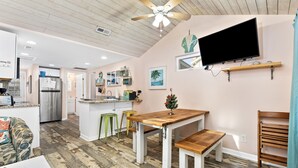 Una cocina moderna con una isla central, mesa de comedor de madera con bancos y un televisor de pantalla plana montado en la pared.