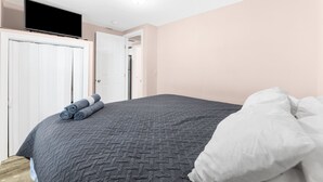 Un dormitorio con una cama, un televisor en la pared y una puerta que da a otra habitación.
