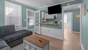 A living room with a gray sofa, a wooden coffee table, and a TV mounted on the wall. - Renovated-Beach Bungalow-Walk to Beach (Hampton)
