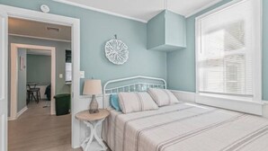 A bedroom with a bed, bedside table, lamp, and a decorative wall piece. - Renovated-Beach Bungalow-Walk to Beach (Hampton)