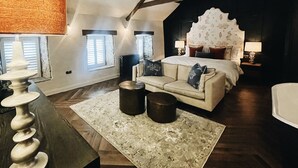 A spacious bedroom with a large bed, a sitting area with a sofa and coffee table, and a view of the outdoors through the windows. - Stylish apartment above popular traditional village pub! (Saint Brides Major)