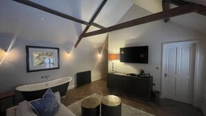 A loft-style room with a high ceiling, exposed beams, a large window, a bathtub, a sofa, a coffee table, a television, and a door. - Stylish apartment above popular traditional village pub! (Saint Brides Major)