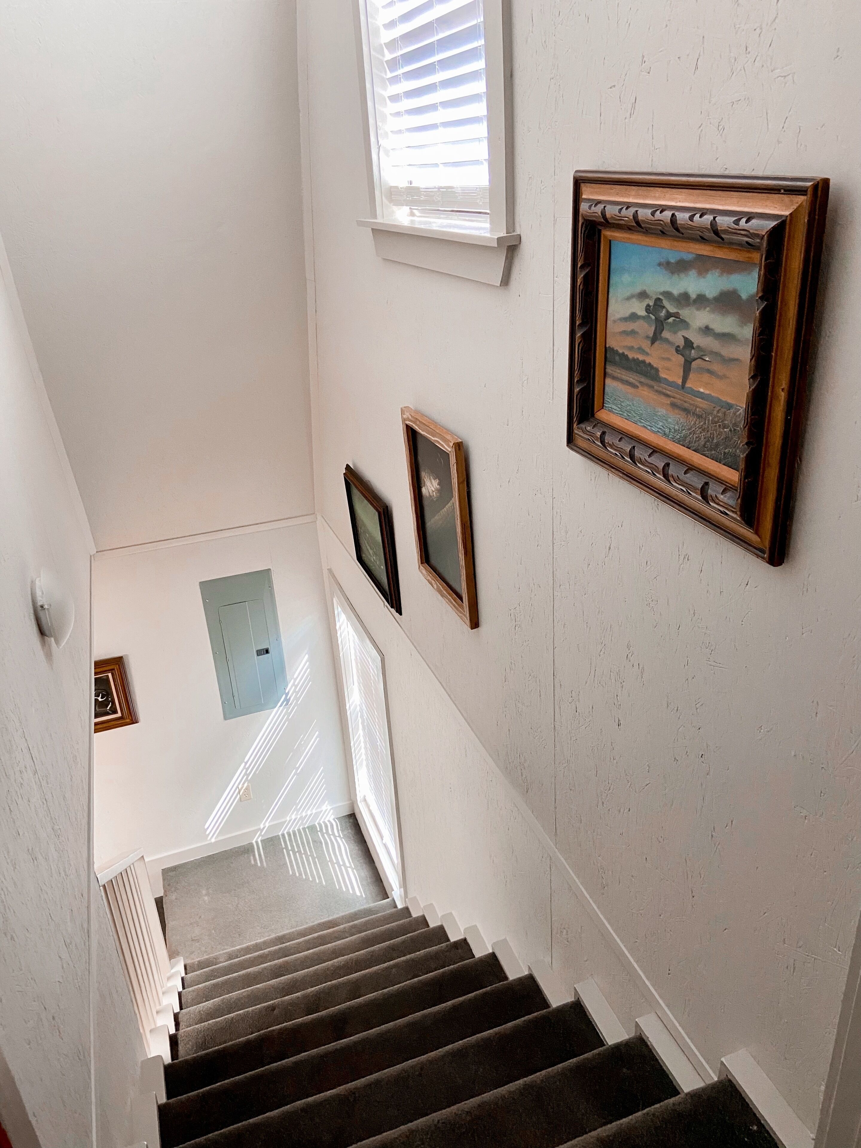 A staircase with a handrail, a light switch, and a framed painting on the wall.
