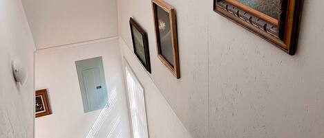 A staircase with a handrail, a light switch, and a framed painting on the wall.