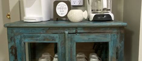 A teal cabinet with a coffee maker, a clock, and a framed picture on the wall above it.