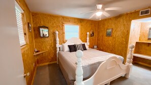 Quarto com cama de dossel branca, paredes de madeira, ventoinha no teto e janela com persianas.