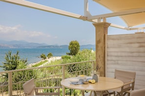 A balcony with a table set for two, overlooking a coastal landscape with mountains in the distance.