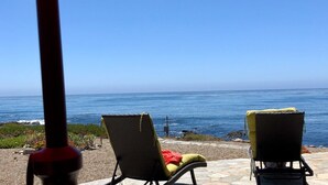 Blick auf einen Strand mit zwei Liegestühlen und einem roten Sonnenschirm.