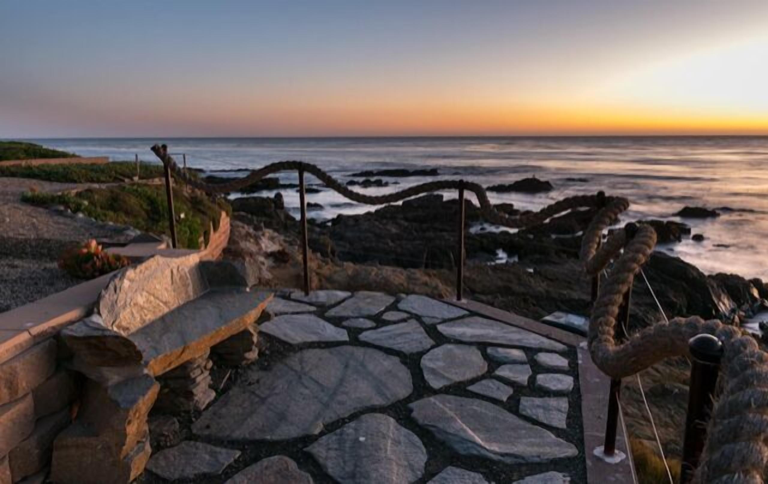 A stone pathway leading to a coastal view with a sunset.