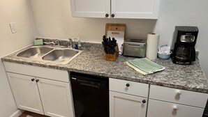 Una cocina con dos fregaderos, un tostador, una cafetera y un escurreplatos.