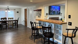 Une cuisine moderne avec un bar en bois, des chaises sombres et un téléviseur diffusant un concert.