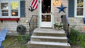 Une maison avec une porte d’entrée, des marches, une boîte aux lettres, une décoration en forme d’étoile bleue et un pot de fleurs.
