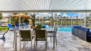 An outdoor pool area with lounge chairs, a table, and a covered seating area. - Waterfront, Heated Pool, Dive In Theater,Family Friendly (Cape Coral)