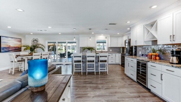 A modern kitchen with white cabinets, a dining area with a table and chairs, and a large window providing natural light. - Waterfront, Heated Pool, Dive In Theater,Family Friendly (Cape Coral)