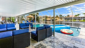 A covered outdoor area with a pool, blue cushioned seating, and a view of the surrounding area. - Waterfront, Heated Pool, Dive In Theater,Family Friendly (Cape Coral)