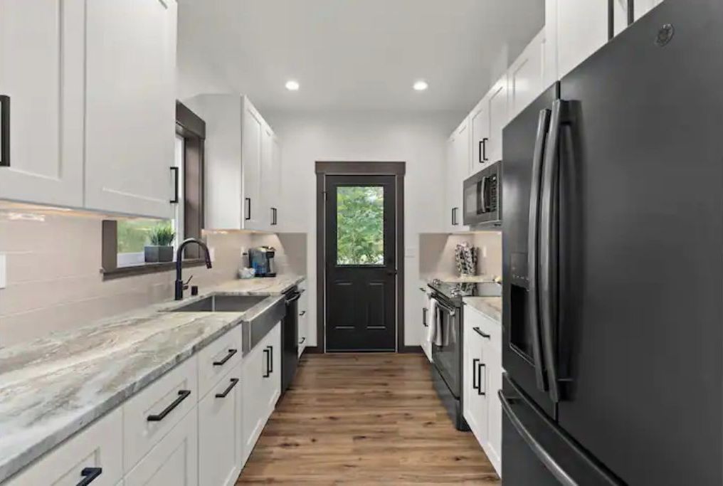 A modern kitchen with white cabinets, a black refrigerator, and a wooden floor.