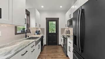A modern kitchen with white cabinets, a black refrigerator, and a wooden floor.