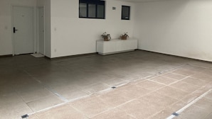 Un espacio amplio y vacío con piso de baldosas, paredes blancas y una pequeña consola blanca con plantas en macetas.