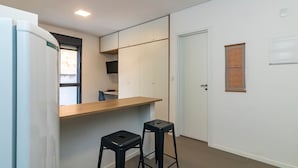 Una cocina compacta con un refrigerador empotrado, una encimera de madera y dos taburetes negros.