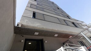 Un edificio de varios pisos con fachada de concreto, una entrada visible con una reja metálica y una escalera que conduce a un nivel superior.