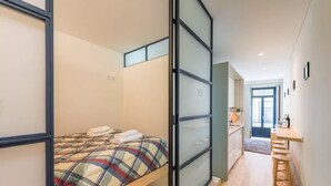 Een slaapkamer met een bed, een schuifdeur en een kitchenette met een aanrecht en krukjes.