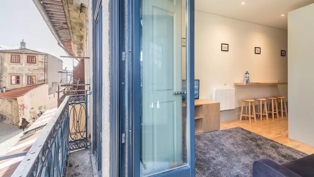 Een modern appartement met balkon, een glazen deur naar een keuken en uitzicht op omliggende gebouwen.
