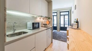 Een moderne keuken met een ingebouwde magnetron, gootsteen en kasten. Er staat een houten bankje en een kleine tafel met een fles erop.