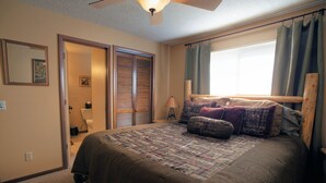 Un dormitorio con una cama grande, un ventilador de techo, una ventana con cortinas y una puerta que da a un baño.