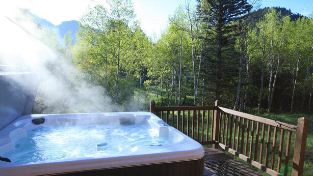 Un jacuzzi en una terraza de madera con un bosque de fondo.