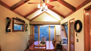 Comedor con mesa y sillas de madera, candelabro y vistas amplias a través de grandes ventanas.
