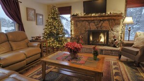 Una sala de estar acogedora con chimenea, sofás de cuero, un árbol de Navidad y un televisor de pantalla plana sobre la chimenea.