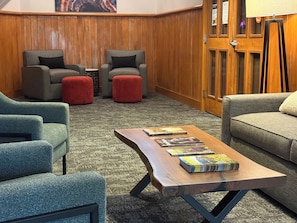 A room with a wooden floor, a wooden door, and a seating area with two armchairs and a sofa.