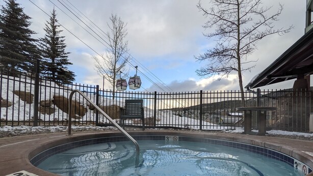 A hot tub with a 3 FT depth limit sign, surrounded by a metal fence, with snow-covered ground and trees in the background.