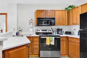 A modern kitchen with wooden cabinets, a stainless steel stove, a microwave, and a dishwasher.