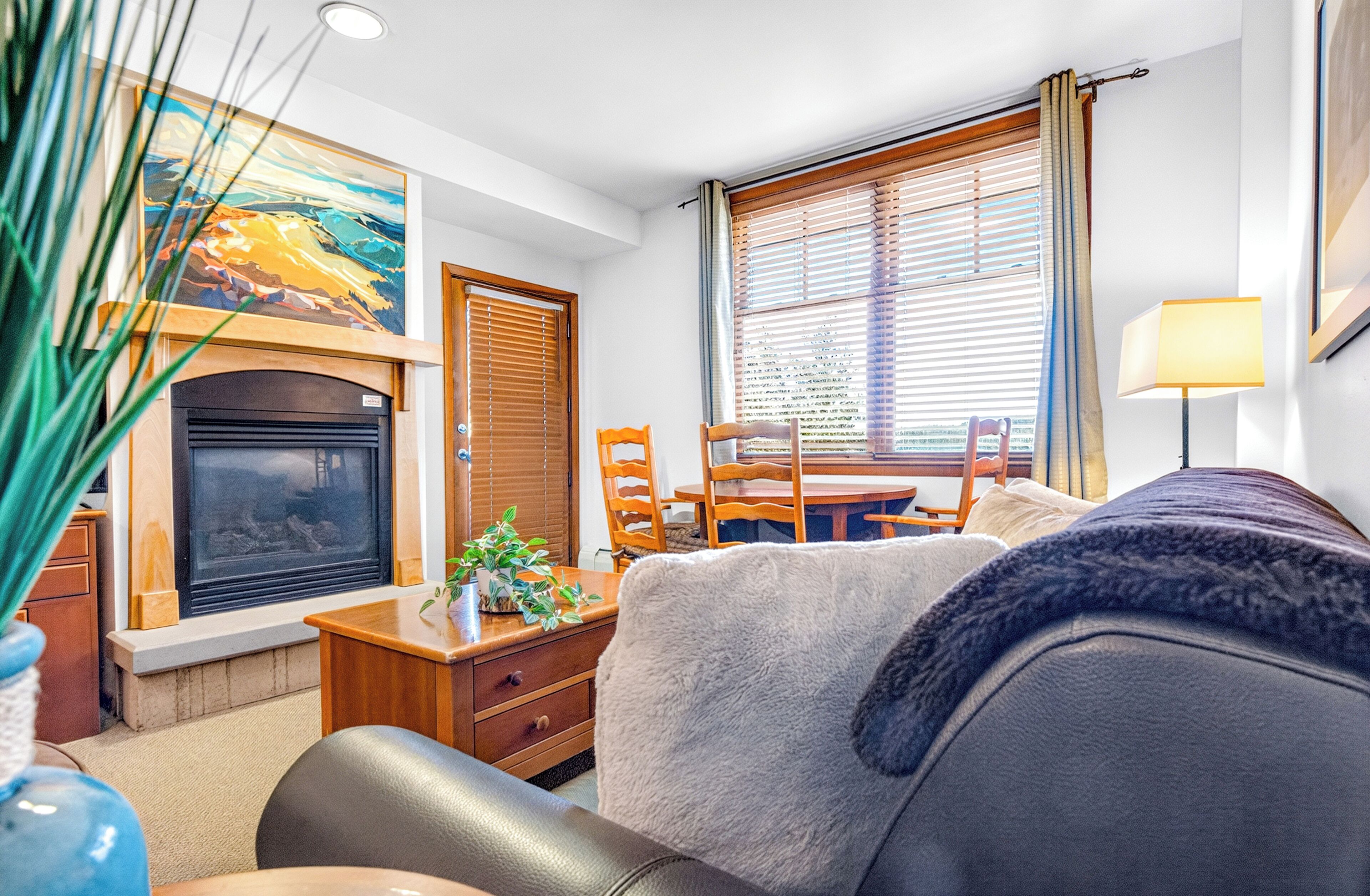 A cozy living room with a fireplace, a dining area, and a large window with blinds.