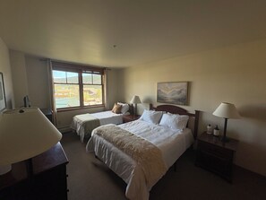 Una habitación de hotel con dos camas, un ventanal con vistas, un cuadro en la pared y lámparas de noche.
