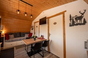 Interior acogedor de una cabaña con techo de madera, un sofá, una mesa de comedor con sillas y un televisor montado en la pared.