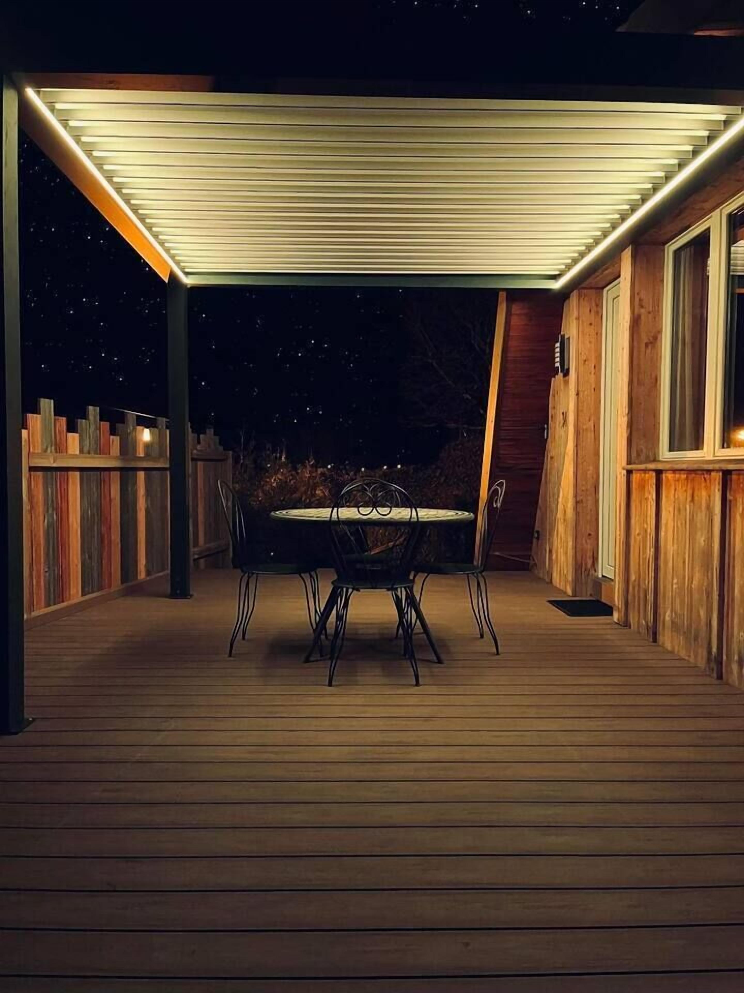 Un patio extérieur couvert avec une table et des chaises, une terrasse en bois et une vue sur le ciel nocturne.