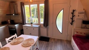 A compact kitchen with a dining area, a large window with curtains, a unique curved door, and a small table with woven placemats. - Nouveau chalet romantique à la montagne avec jacuzzi et sauna privatif (Métabief)